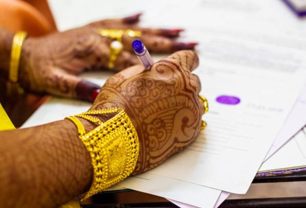 a newly married indian bengali wife with golden ornament and blacelet signing marriage registration form